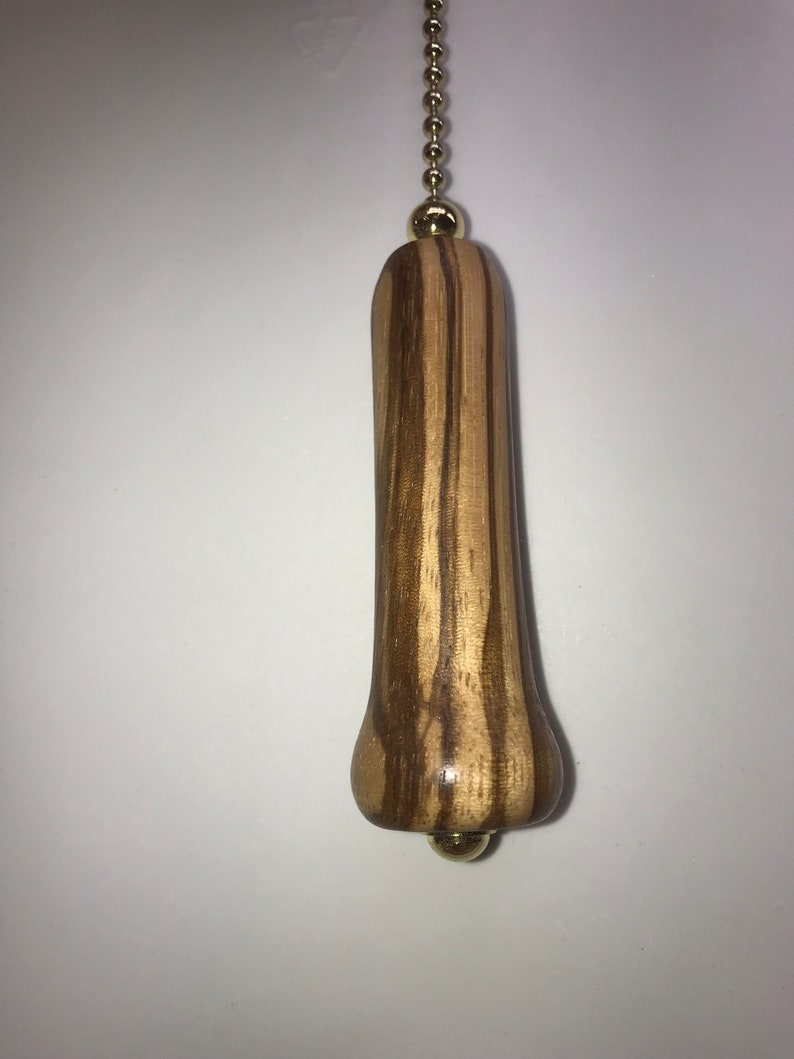 K&ouml;nnte beinhalten: Ein Holz-L&uuml;fterzug mit einem braunen und hellbraunen Streifenmuster. Der Zug hat eine goldene Kette und eine goldene Kugel oben und unten.
