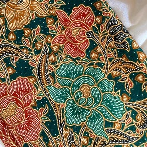 May include: Close-up of a fabric with a floral pattern. The design features large flowers in red, brown, and teal, with white dotted details, set against a dark green background. The fabric has a detailed, ornate look.