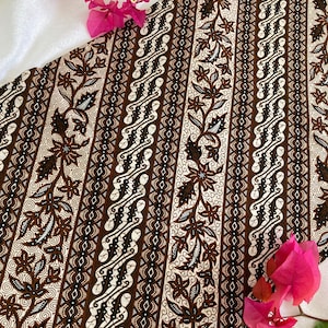 May include: Brown and white batik fabric with a floral pattern. The fabric has a diagonal stripe pattern with a repeating floral design. The fabric is shown on a white surface with pink flowers.