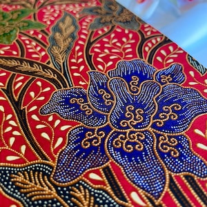 May include: Red fabric with a blue floral pattern. The fabric is decorated with small gold and silver beads. The pattern is reminiscent of traditional Indonesian batik.