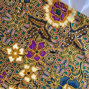 May include: Close-up of a fabric with a detailed floral pattern. The design features flowers in shades of purple, white, and teal, set against a gold and green background. Black and gold leaf-like shapes are also present, creating a rich, textured look.