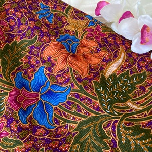 Puede incluir: Tela morada con un patrón floral con flores naranjas, azules, verdes y doradas. La tela tiene un diseño batik tradicional.