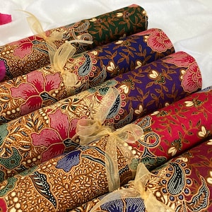 May include: Six rolls of fabric with different colorful floral patterns. The fabric is tied with a gold ribbon and has a brown background.