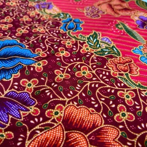 May include: A close-up of a red and burgundy fabric with a floral pattern. The fabric features a variety of flowers in shades of blue, purple, orange, and pink. The flowers are surrounded by green leaves and vines.