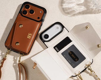 Puede incluir: Dos fundas de teléfono de cuero con ranuras para tarjetas y correas cruzadas. Una funda es marrón con las iniciales doradas "SB", la otra es blanca. Ambas fundas tienen un borde negro y herrajes dorados. Una funda está abierta, revelando una tarjeta de crédito.