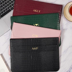 May include: Four rectangular laptop sleeves with a crocodile-embossed texture, stacked vertically. The sleeves are burgundy with AKLY, dark green with V♥L, light pink with C|W, and black with A&F embossed in gold lettering on the front flaps.
