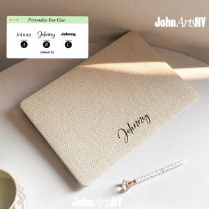 May include: A beige textured laptop case featuring the name Johnny in black script font. An overlay displays personalisation options with three font styles labelled A, B, and C. A white pen with a diamond-shaped topper rests nearby.
