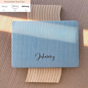 May include: A light blue laptop case with a textured crocodile skin pattern and the name Johnny printed in black script. Above the case, a text chart displays three font options labeled F1, F2, and F3 with the name Johnny in each style.