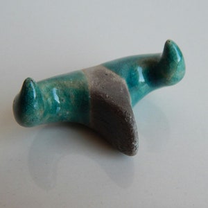 K&ouml;nnte beinhalten: Eine teal- und graue Keramikskulptur mit zwei spitzen Enden. Die Skulptur ist abstrakt und hat eine glatte, glasierte Oberfl&auml;che.