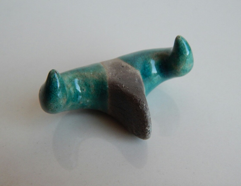K&ouml;nnte beinhalten: Eine teal- und graue Keramikskulptur mit zwei spitzen Enden. Die Skulptur ist abstrakt und hat eine glatte, glasierte Oberfl&auml;che.