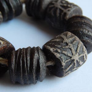 May include: A close-up of a bracelet made of dark brown ceramic beads. The beads have a textured surface and some have a geometric pattern.