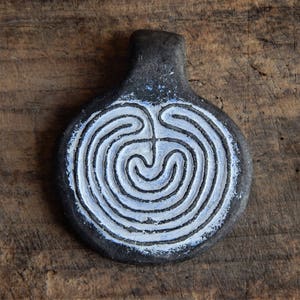Könnte beinhalten: Ein schwarzer Keramik-Anhänger mit einem weißen, bemalten Labyrinth-Design. Der Anhänger hat oben eine Schlaufe zum Aufhängen.