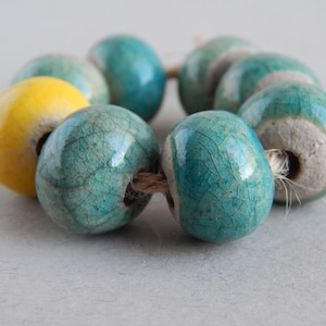 May include: A strand of ceramic beads in shades of teal and yellow. The beads are strung on a natural twine cord.