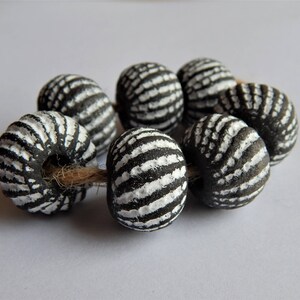 May include: A strand of black and white striped ceramic beads. The beads are round and have a textured surface.