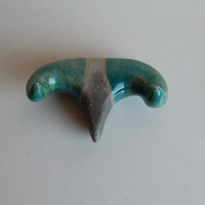 K&ouml;nnte beinhalten: Eine Keramikskulptur in Form eines stilisierten Vogels mit gr&uuml;ner und grauer Glasur.