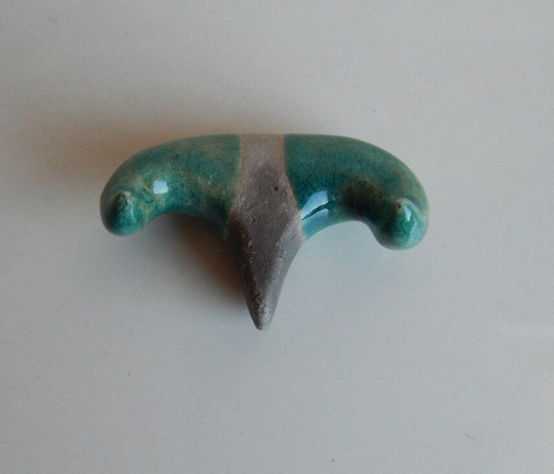 K&ouml;nnte beinhalten: Eine Keramikskulptur in Form eines stilisierten Vogels mit gr&uuml;ner und grauer Glasur.