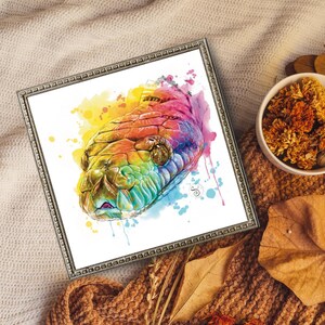 Op de afbeelding: Een ingelijste aquarelprint met een kleurrijke slangenkop. Het kunstwerk toont een levendig palet van regenboogkleuren, met spetters van geel, blauw en roze. De schubben van de slang zijn gedetailleerd en de lijst heeft een zilveren afwerking.