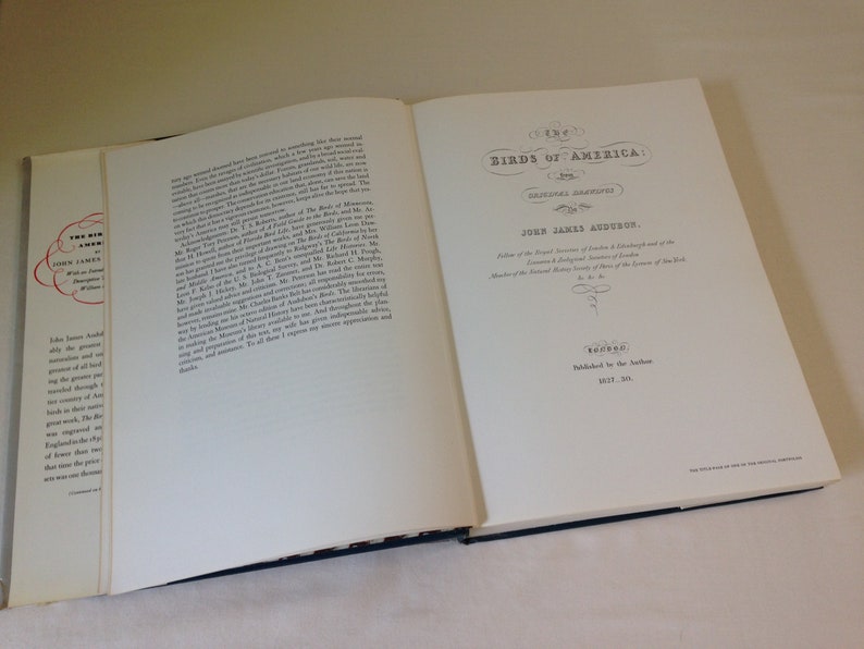 May include: A white book with the title "Birds of America" in black lettering. The book is open to the title page, which includes the author's name, John James Audubon, and the date 1827-38.
