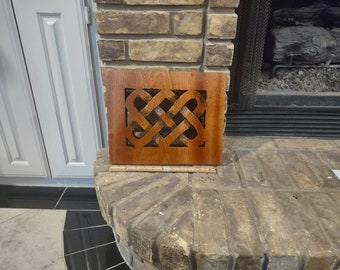 May include: A wooden vent cover with a Celtic knot design. The cover is stained a dark brown color and has a rectangular shape.
