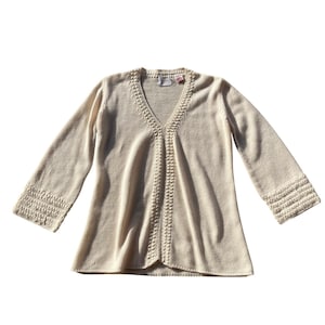 May include: Cream-colored sweater with a V-neck and three-quarter sleeves. The sweater features a decorative knit pattern down the center and on the sleeve cuffs. A small tag is visible near the neckline.
