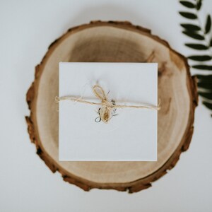 May include: A white gift box tied with twine and a small sprig of greenery, sitting on a wooden slice.