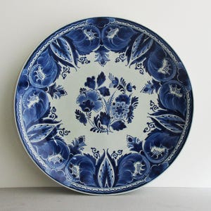 May include: A round, white ceramic plate with a blue floral design. The plate features a central floral bouquet and a border of stylized leaves and scrolls. The blue and white color scheme gives the plate a classic, elegant look.