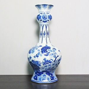 May include: A white ceramic vase with a blue and white floral design. The vase has a wide base and a narrow neck. The floral design is intricate and detailed.