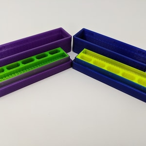 May include: Two 3D printed storage boxes with removable trays. The boxes are purple and blue, and the trays are green. The trays have multiple compartments.