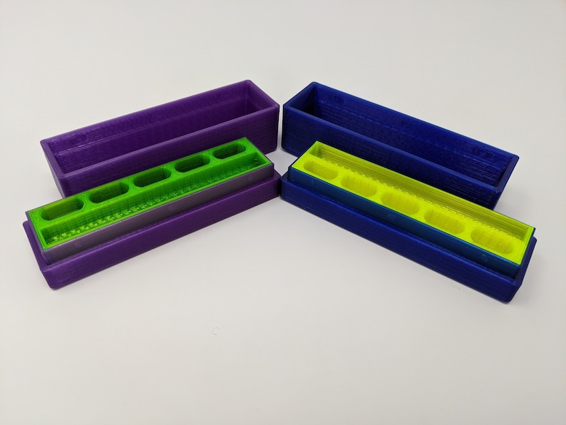 May include: Two 3D printed storage boxes with removable trays. The boxes are purple and blue, and the trays are green. The trays have multiple compartments.