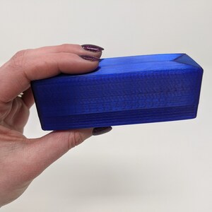 May include: A small, rectangular box made of blue plastic. The box has a smooth, glossy finish and is slightly angled on the top and bottom.