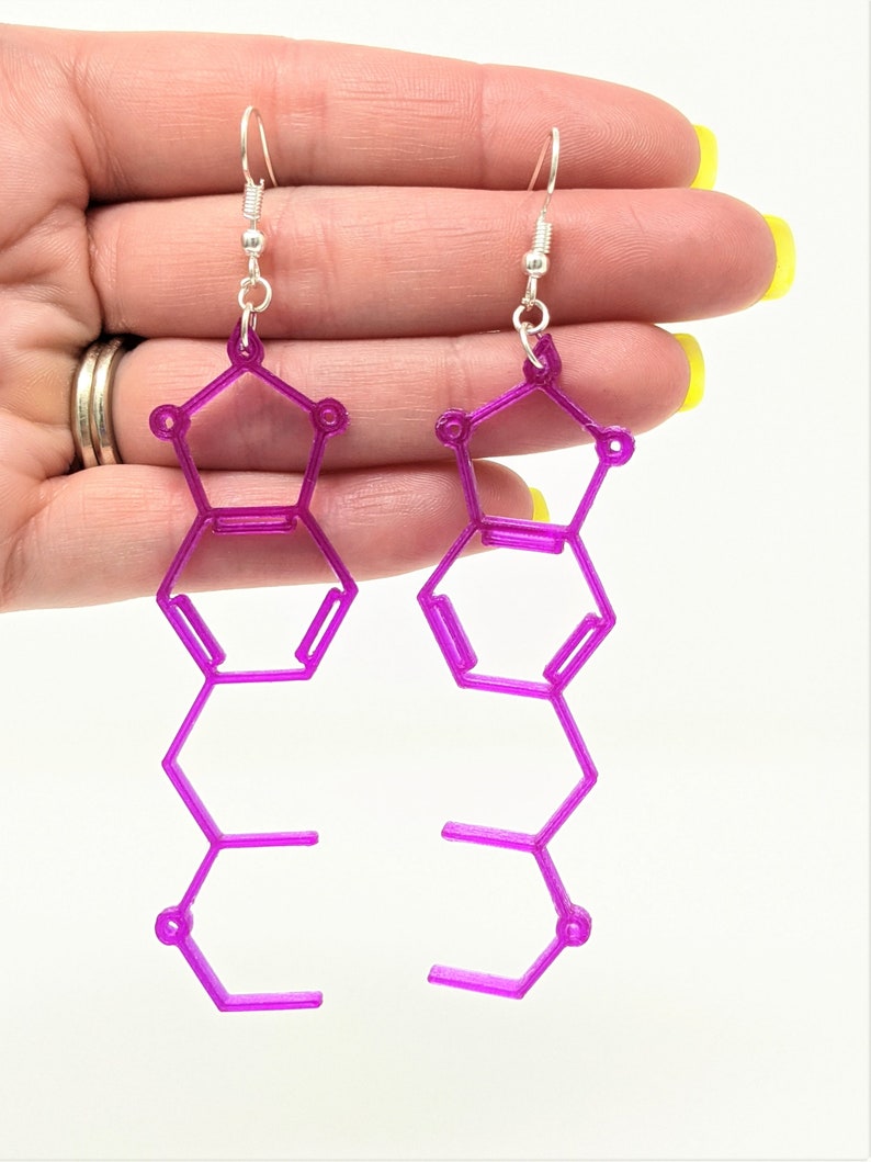 May include: A pair of purple earrings shaped like a chemical structure. The earrings are made of a 3D printed material and have silver hooks.