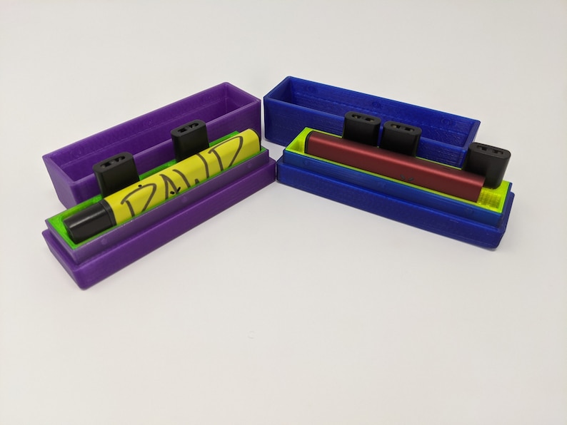 May include: Two 3D printed cases for vape pens. One case is purple with a yellow vape pen that says "D.A.L.I.Z." The other case is blue with a red vape pen.