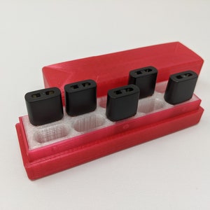 May include: A red plastic case with six black rectangular compartments for holding small items. The case is open and the compartments are empty.