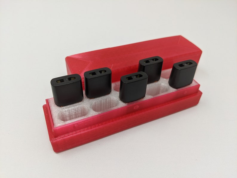 May include: A red plastic case with six black rectangular compartments for holding small items. The case is open and the compartments are empty.