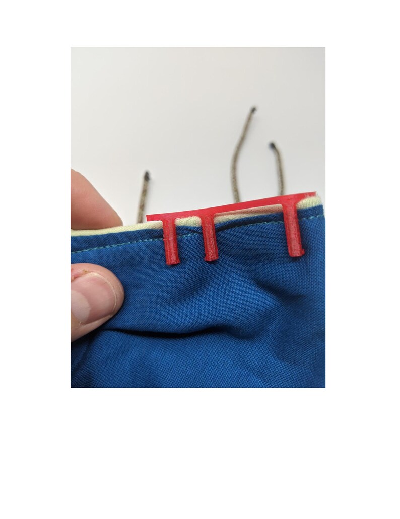 May include: Red plastic mask strap adjusters with three prongs, attached to a blue fabric face mask with a beige lining.
