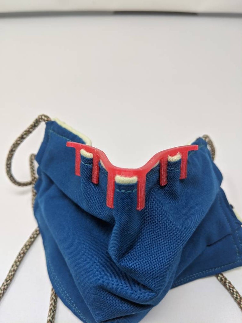 May include: A red plastic face mask brace with four prongs, designed to help keep a cloth face mask from collapsing in on the wearer's nose and mouth.