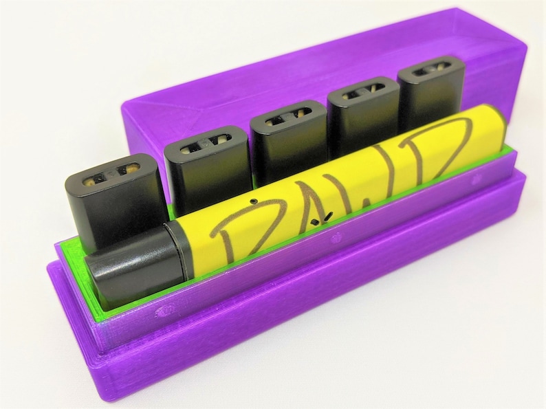 May include: A purple case with a green liner holds five black vape cartridges and a yellow vape pen with the word "DAWD" written on it.