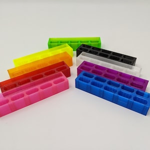 May include: A set of eight colorful 3D printed organizers, each with a different color: green, yellow, orange, red, pink, purple, white, and blue. The organizers are arranged in a staggered pattern, with the green organizer at the top and the blue organizer at the bottom.