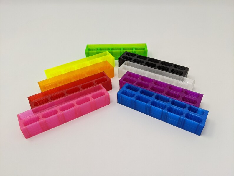 May include: A set of eight colorful 3D printed organizers, each with a different color: green, yellow, orange, red, pink, purple, white, and blue. The organizers are arranged in a staggered pattern, with the green organizer at the top and the blue organizer at the bottom.