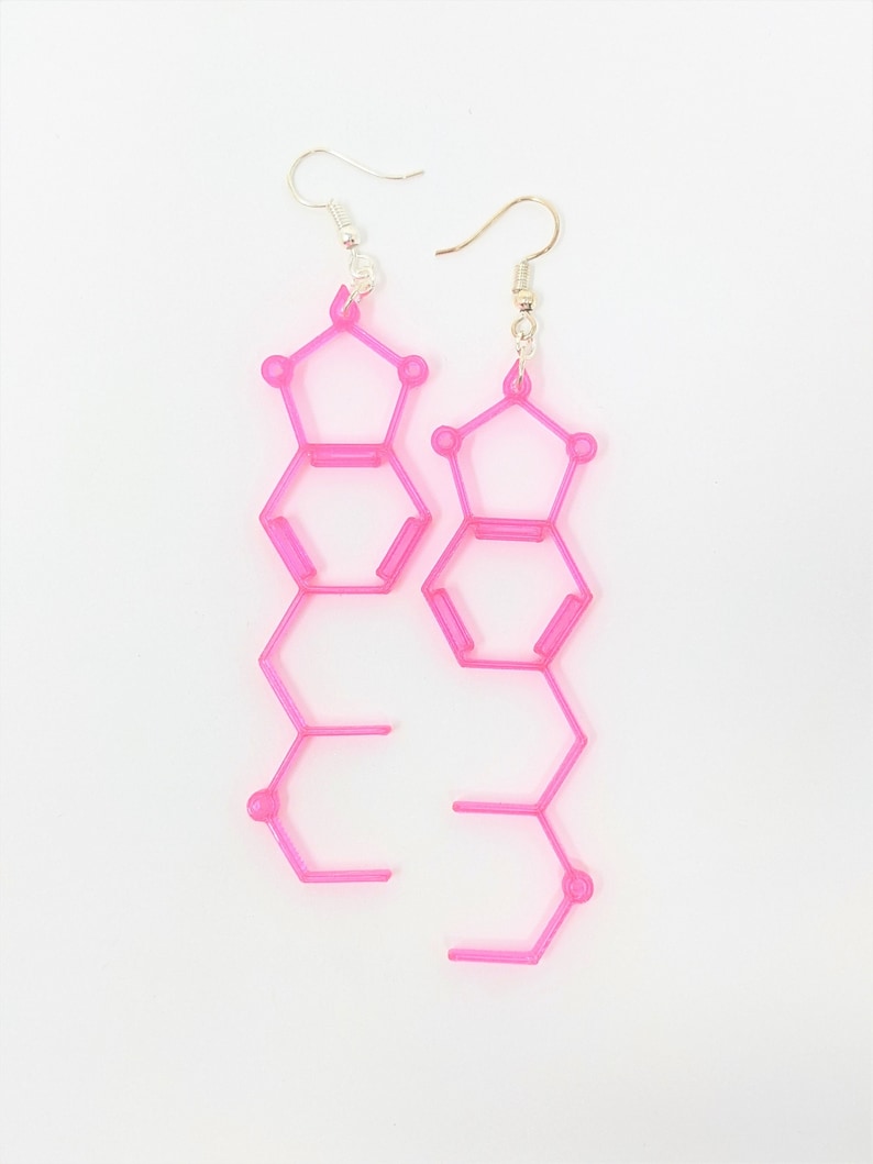 May include: A pair of pink dangle earrings with a geometric design. The earrings are made of plastic and have a silver hook.