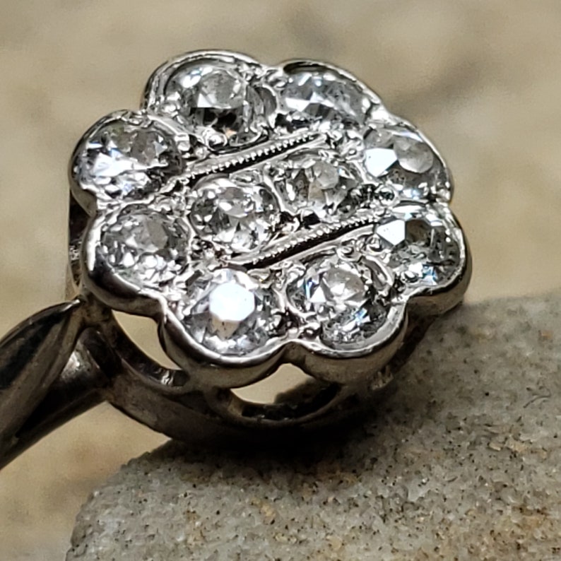 May include: A silver ring with a flower-shaped setting featuring a cluster of small, round, clear diamonds.