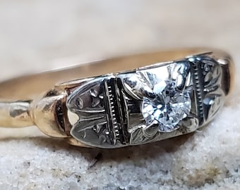Può includere: Un anello vintage in oro e argento con un singolo diamante rotondo incastonato al centro. L'anello presenta un intricato design floreale.