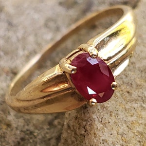 Puede incluir: Un anillo de oro con una gema de rub&iacute; ovalada. El anillo tiene una banda de oro pulido y un engaste que sujeta firmemente la piedra roja vibrante. Una joya cl&aacute;sica.
