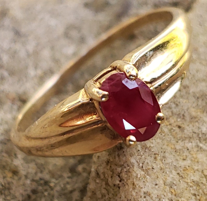 Puede incluir: Un anillo de oro con una gema de rub&iacute; ovalada. El anillo tiene una banda de oro pulido y un engaste que sujeta firmemente la piedra roja vibrante. Una joya cl&aacute;sica.