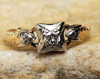 Può includere: Un anello di fidanzamento vintage in oro bicolore con un singolo diamante rotondo incastonato in una montatura a griffe quadrata. L'anello presenta intricati dettagli floreali sulla fascia.
