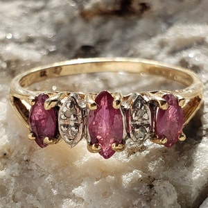 May include: A gold band ring featuring three pink marquise-shaped gemstones and two smaller round diamonds.