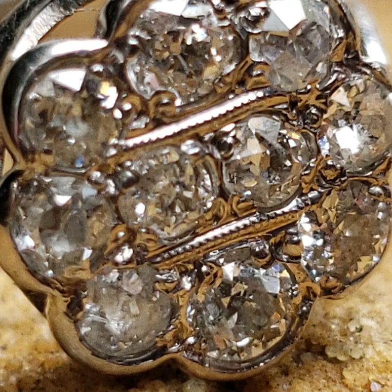 May include: A silver ring with a cluster of small, round, clear diamonds set in a flower-shaped design.