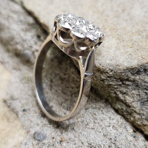 May include: A silver ring with a cluster of small, clear stones set in a delicate, floral design.