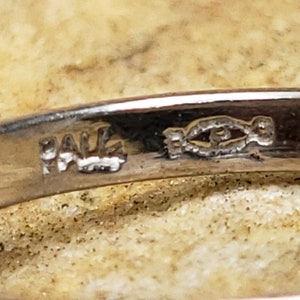 May include: Close-up of a silver ring with the inscription "PALE" and a stylized fish design.