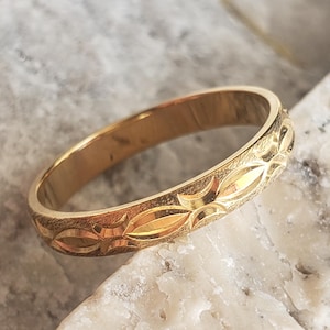 Peut inclure: Une bague anneau en or présentant un motif répétitif de formes en losange allongées et polies sur un fond texturé au fini mat. L'anneau possède une largeur constante et une surface intérieure lisse et réfléchissante.
